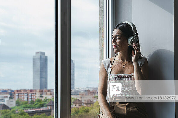 Young businesswoman listening to music on headphones by window at work place
