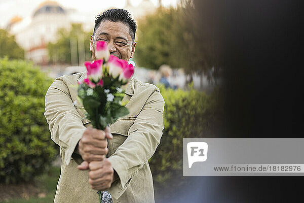 Smiling mature man showing flowers in park on Valentine's day