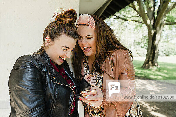 Two laughing friends looking at cell phone
