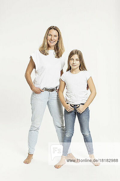 Mother and daughter with hands in pockets against white background