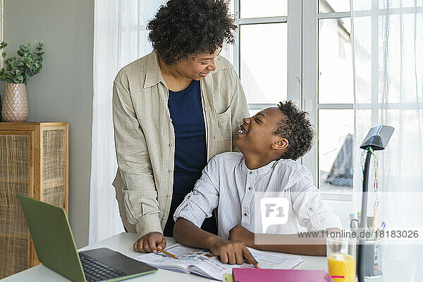 Happy mother talking to son sitting at study table in home