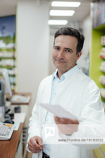 Smiling pharmacist showing prescription at store