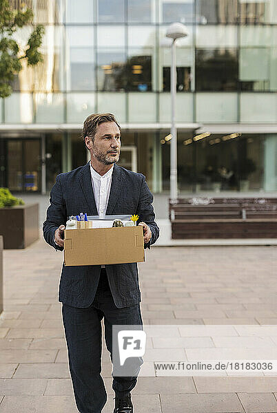 Businessman carrying cardboard box in front of office building