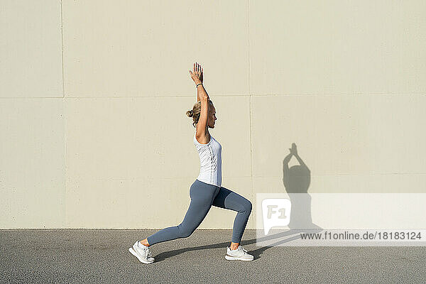 Woman practicing Ashta Chandrasana in front of wall on sunny day
