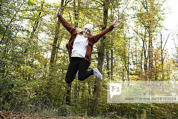 Carefree mature woman jumping in front of trees at forest