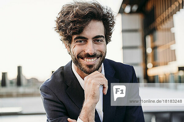Happy young businessman with hand on chin