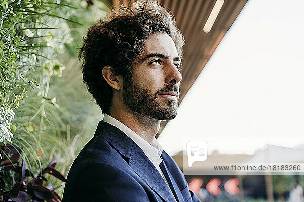 Handsome young businessman day dreaming near plants