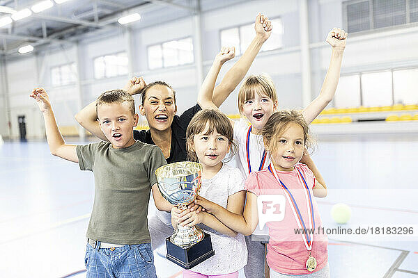 Teacher cheering with students holding trophy at school sports court