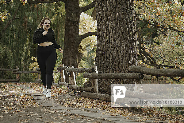 Smiling plus sized woman jogging in autumn park