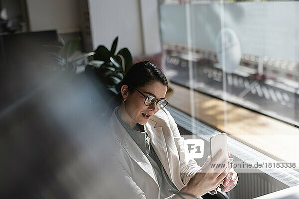 Geschäftsfrau mit Brille macht im Büro ein Selfie mit dem Mobiltelefon