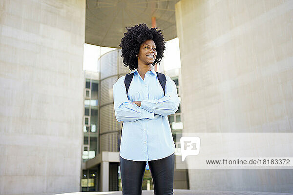 Happy young businesswoman standing with arms crossed amidst wall