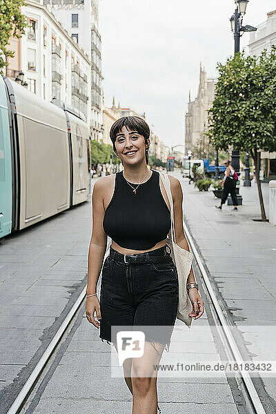 Smiling young woman with short hair walking at tramway on street