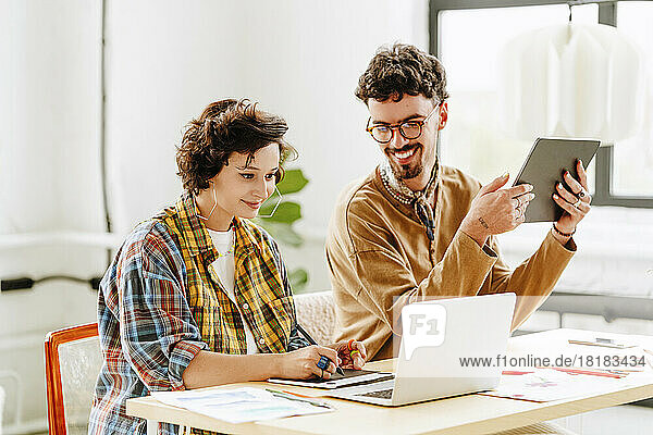 Happy illustrator with colleague using graphics tablet and laptop at desk