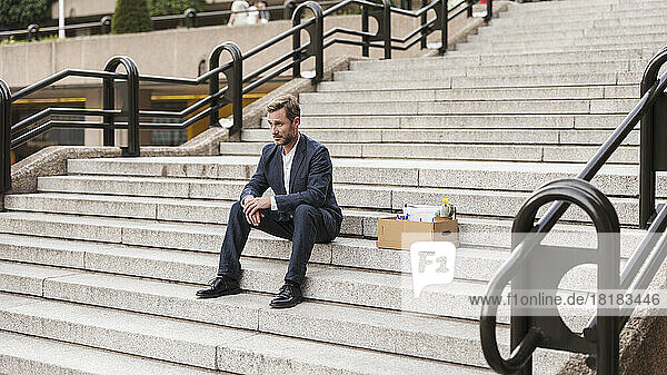 Businessman sitting with cardboard box on steps