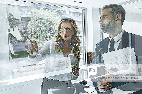 Businesswoman explaining to colleague using sticky notes in office