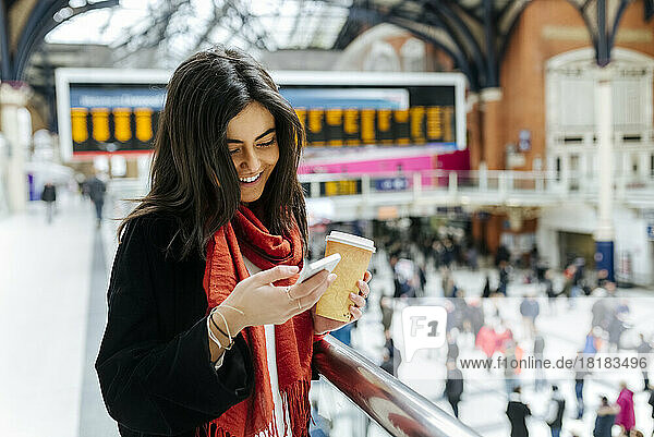 UK  London  Young woman using mobile phone at train station