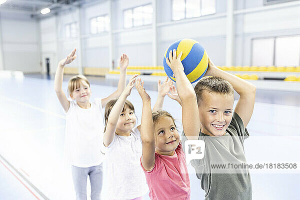Smiling schoolboy passing ball to friends in line at sports court