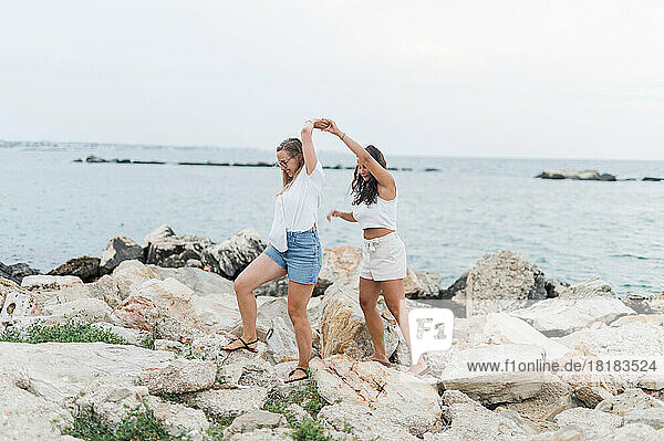 Freunde halten sich an den Händen und gehen gemeinsam auf einem Felsen am Strand spazieren