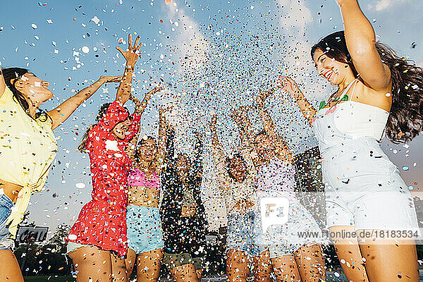 Happy female friends throwing confetti under sky at dusk