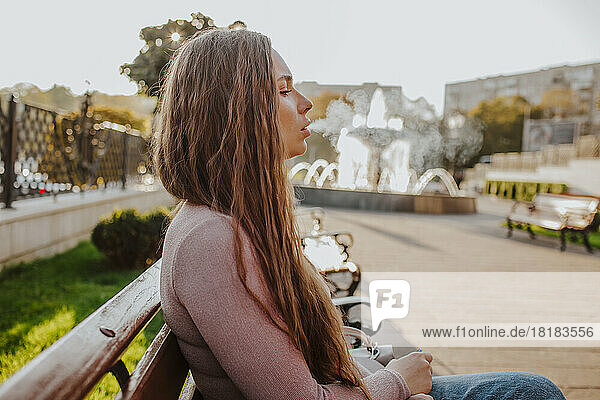 Woman with long hair smoking electronic cigarette on bench