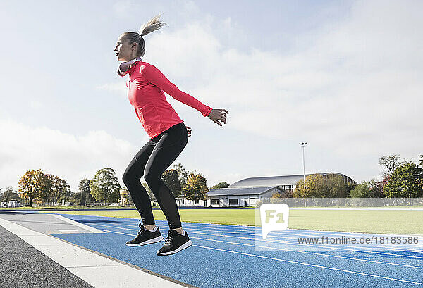 Sportswoman with wireless headphones doing jumping exercise on running track