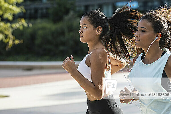 Young woman with friend running on sunny day
