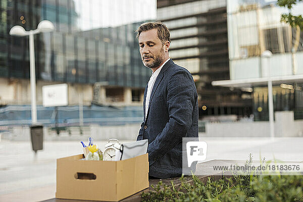 Geschäftsmann sitzt mit Karton vor Bürogebäude