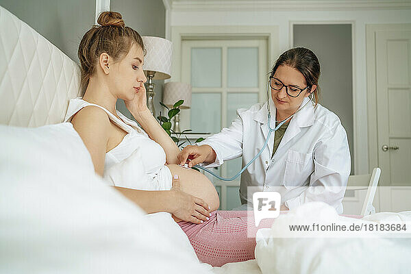 Doctor examining pregnant woman sitting on bed at home