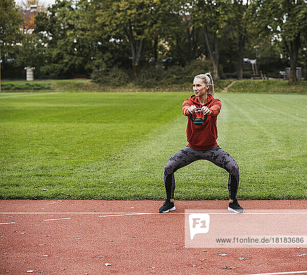Young sportswoman practicing with kettle bell on running track