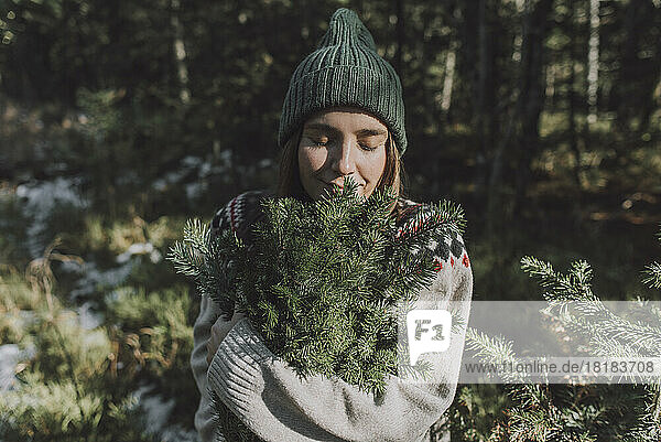 Woman with eyes closed smelling twigs of evergreen tree in forest