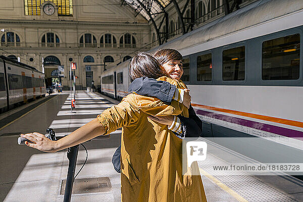 Happy woman with push scooter embracing friend at station