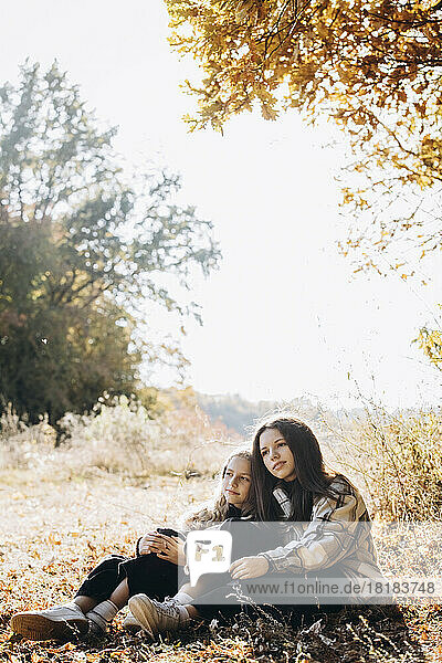 Girl sitting with sister in autumn forest