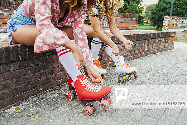 Women sitting on wall tying lace of roller skates