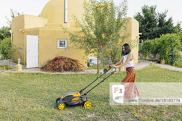 Mature woman mowing backyard lawn
