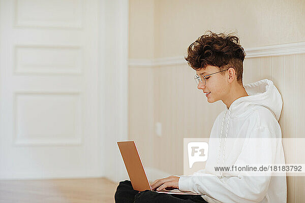Smiling boy using laptop at home by wall