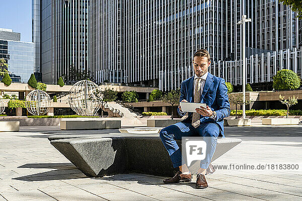 Geschäftsmann sitzt mit Tablet-PC auf Bank im Büropark