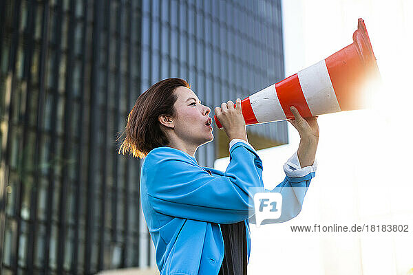 Businesswoman talking using traffic cone on sunny day