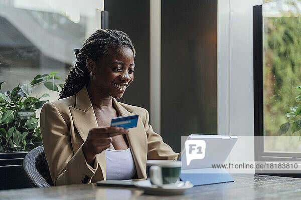 Happy businesswoman holding credit card and using tablet PC at cafe