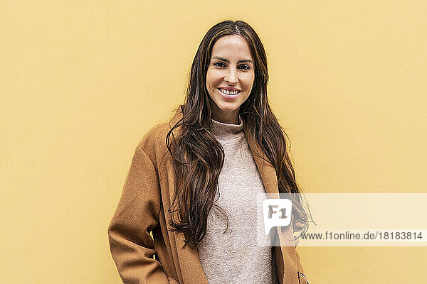 Smiling young woman with long hair in front of yellow wall