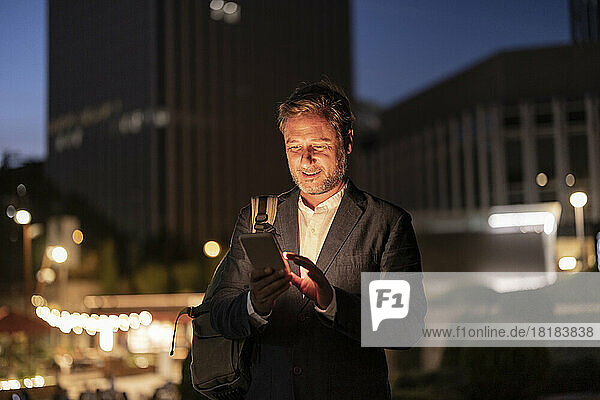 Smiling businessman using mobile phone in city at night