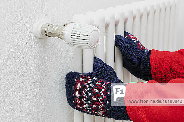 Hands of man wearing woolen glove on radiator