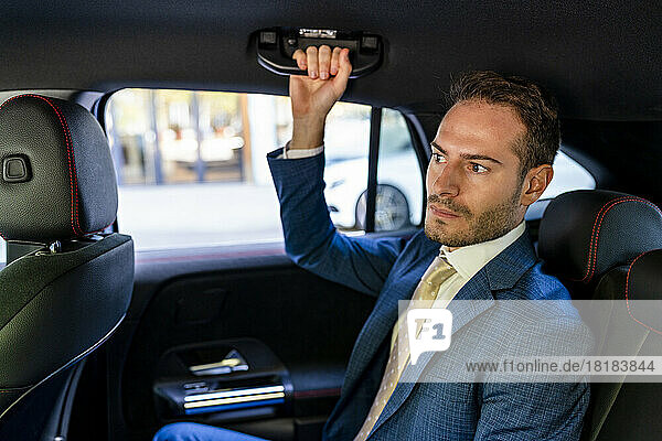 Businessman holding handle sitting in taxi