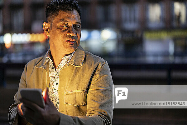 Mature man holding smart phone at night
