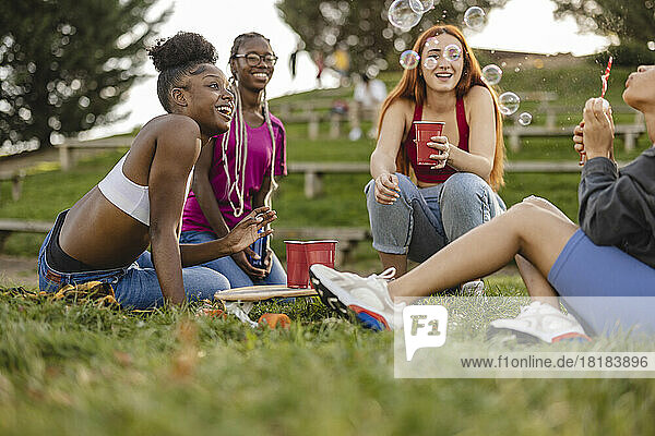 Happy woman blowing bubbles with friends enjoying at park