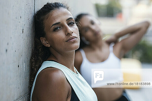 Young woman leaning on wall with friend standing in background
