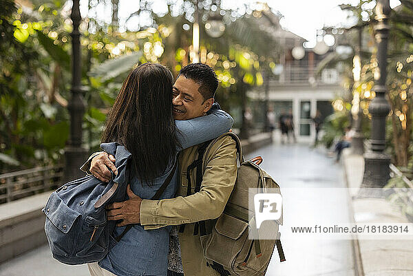 Glücklicher Mann mit Rucksack umarmt Frau im Park