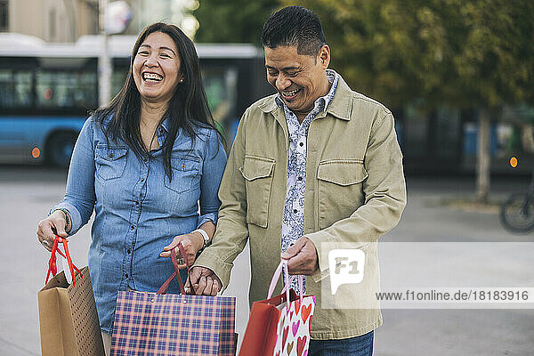 Happy man and woman with shopping bags on footpath