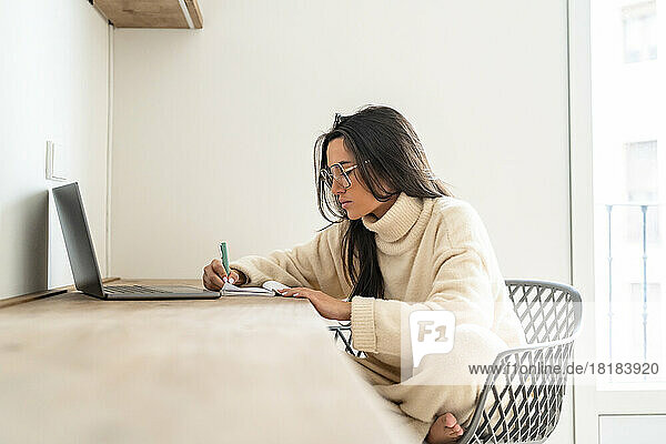 Junge Frau schreibt Tagebuch und arbeitet im Heimbüro