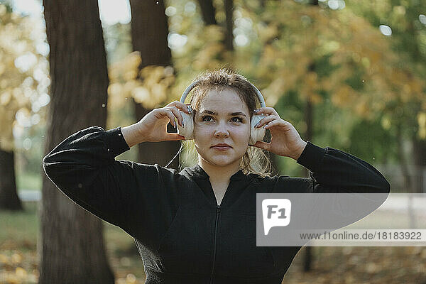 Smiling young woman listening to music through wireless headphones in park