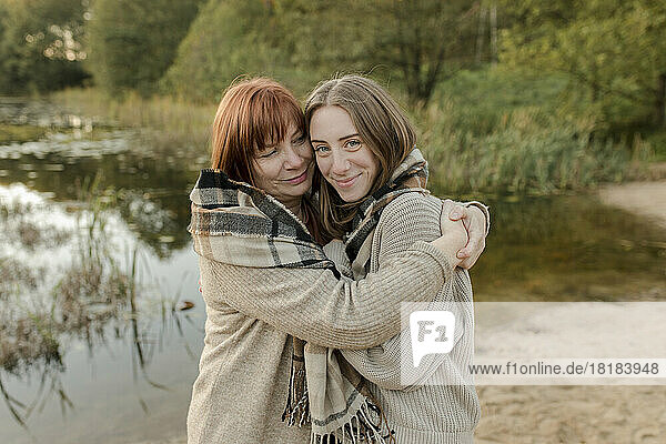 Mutter umarmt Tochter im Pullover in der Nähe des Sees